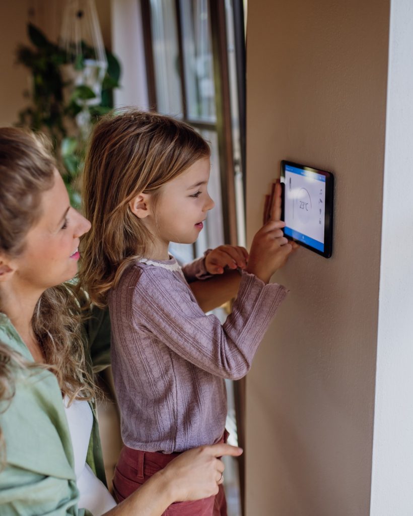 Girl helping mother to adjust, lower heating temperature on thermostat. Concept of sustainable