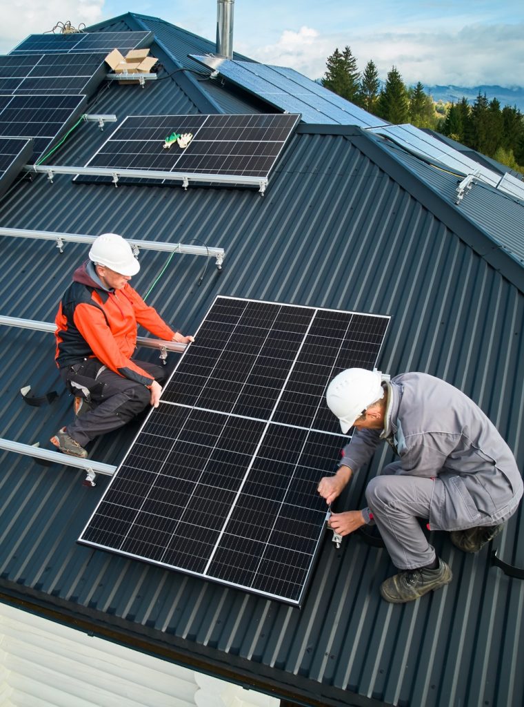 Technicians installing photovoltaic solar panels on roof of house.